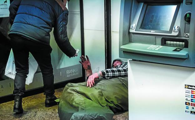 Un voluntario ofrece comida a un ciudadano que duerme en un cajero de San Sebastián en el marco de una campaña de ayuda a los sin techo.