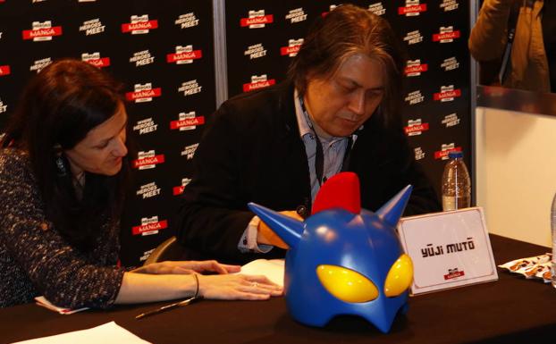 Yuji Muto firma autógrafos con un casco original de Ultrahéroe en la mesa.